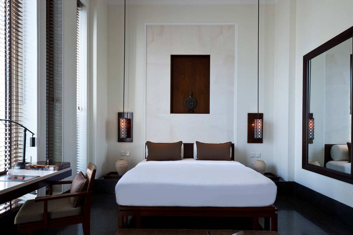 Blick auf das Bett, einen kleinen Schreibtisch und den großen Wandspiegel in einem Deluxe Room des The Chedi Muscat