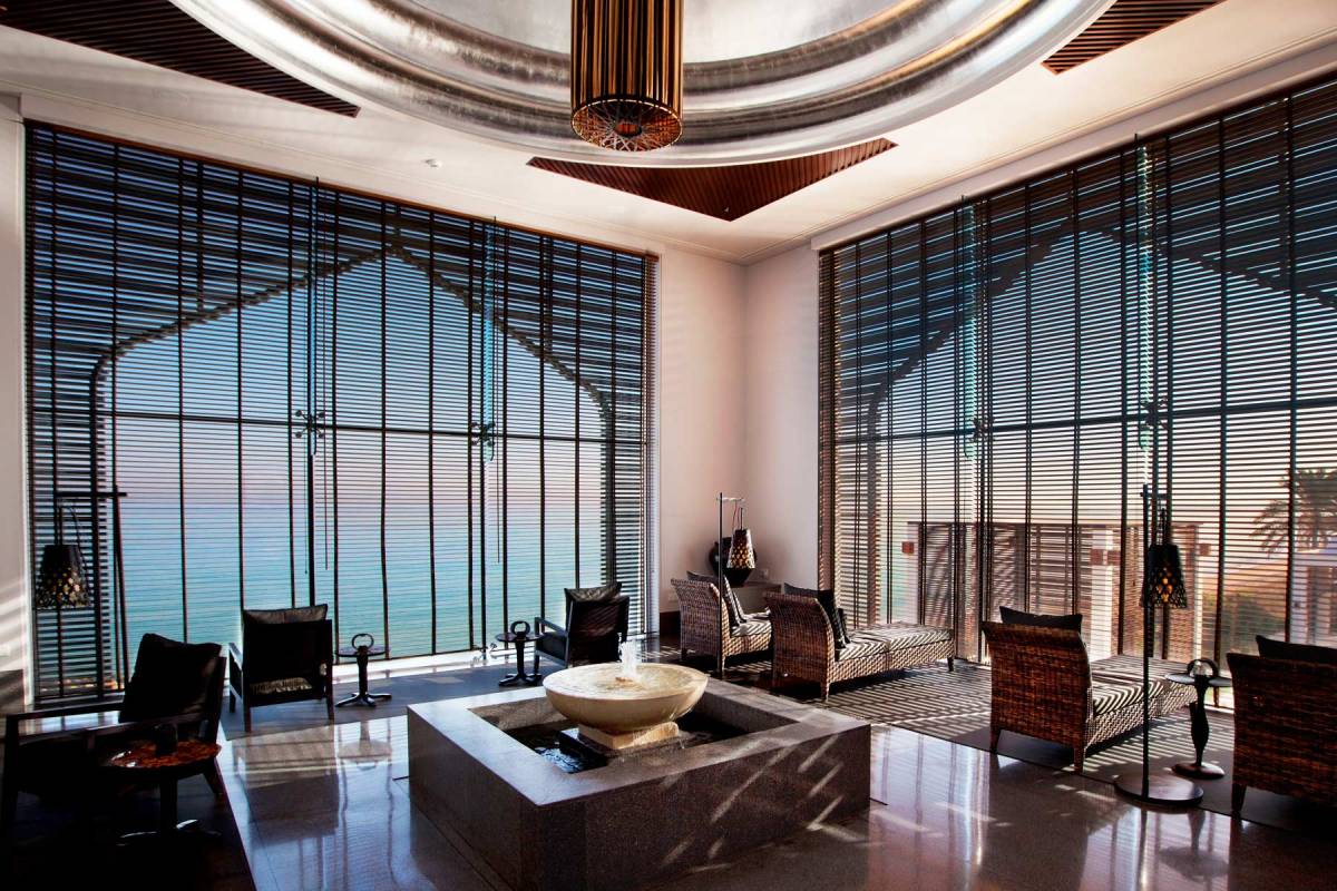 View into the Relax Room of the spa at chedi muscat, with a little water fountain in the middle of the room, relax chairs and big, ground-lever windows which open the view towards the sea