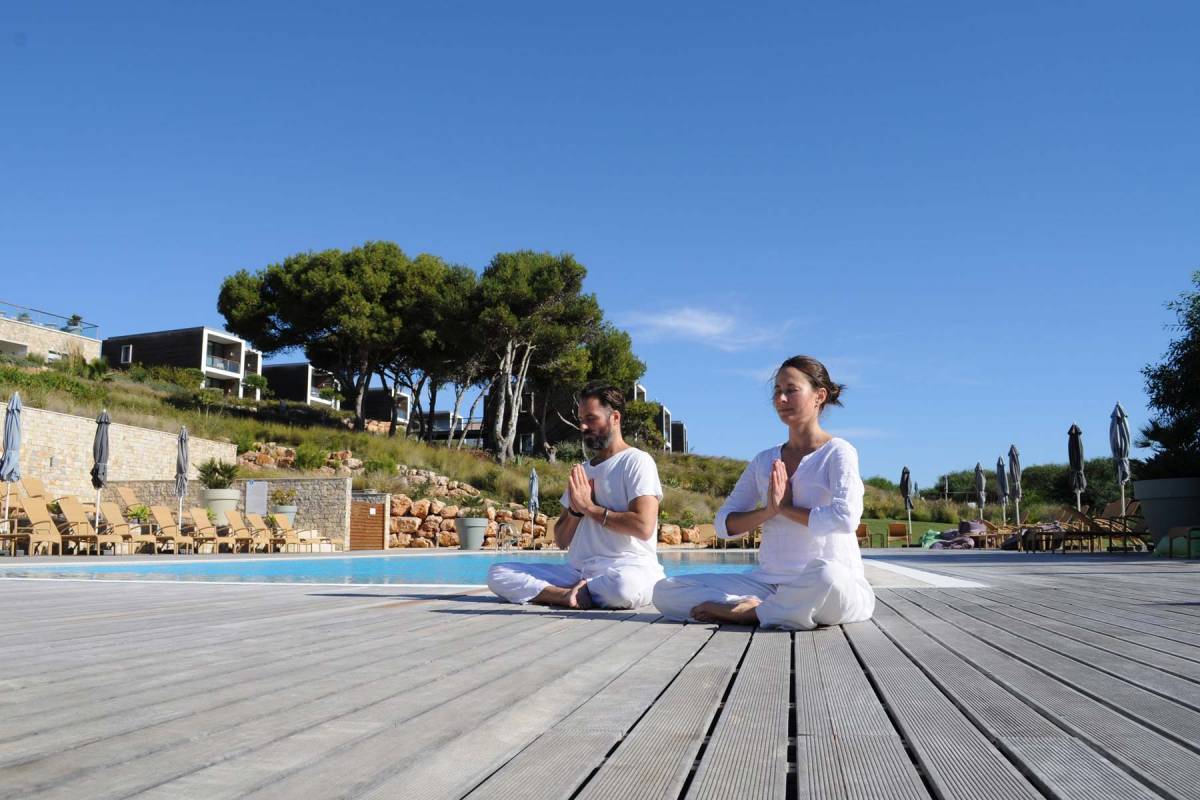 A man and a woman sitting cross legged in the iconic yoga pose near the pool