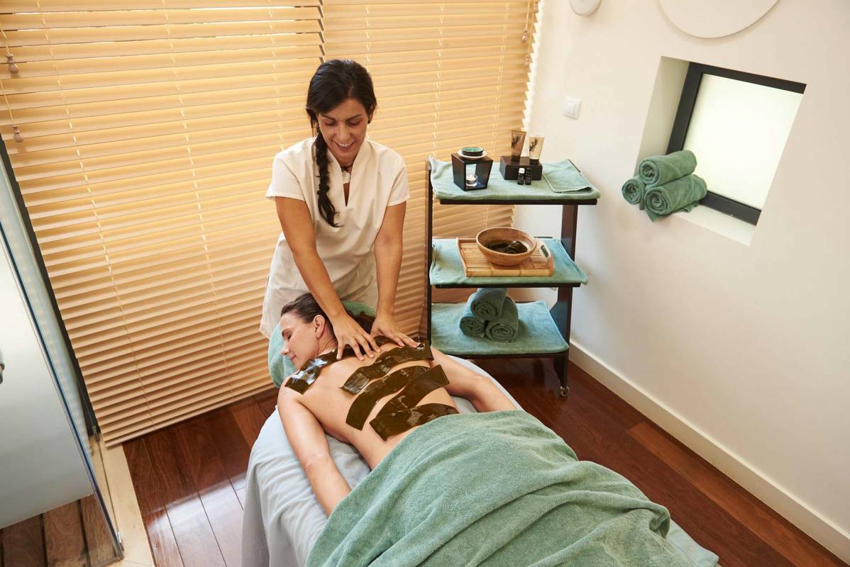 A employee of the spa laying seaweed strips on the back of a hotel guest during a treatment